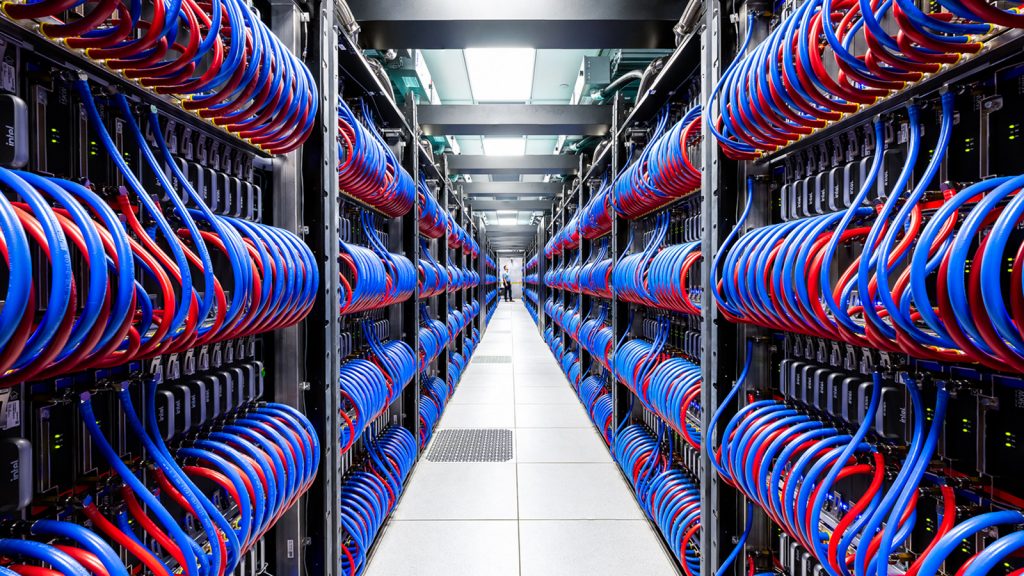 A row from the Aurora super computer. A researcher stands off in the distance looking at cooling cables.