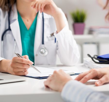 A stock image of a doctor and her patient sitting at a desk going over some papers.