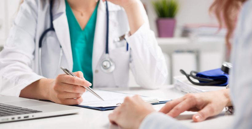 A stock image of a doctor and her patient sitting at a desk going over some papers.