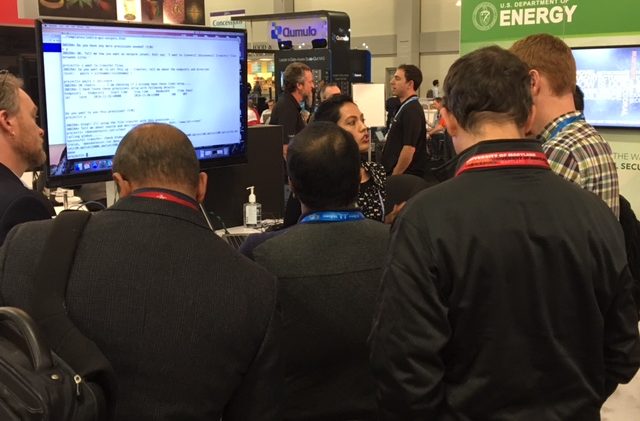 A group stands at the DOE booth watching a demonstration.